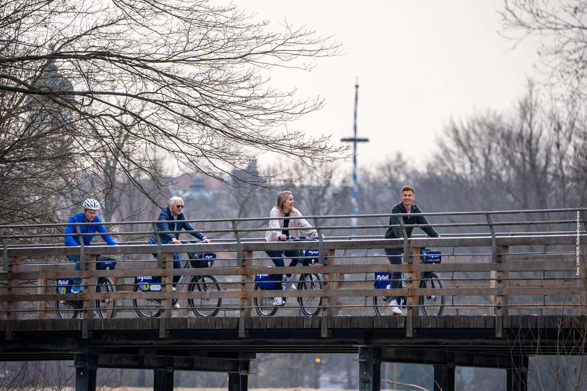 Vier Menschen fahren mit ihren MyRadl Leihrädern hintereinander über eine Brücke.